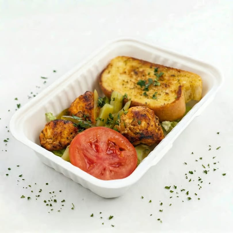 Grilled chicken, sliced tomato, and garlic bread in a white takeout container.