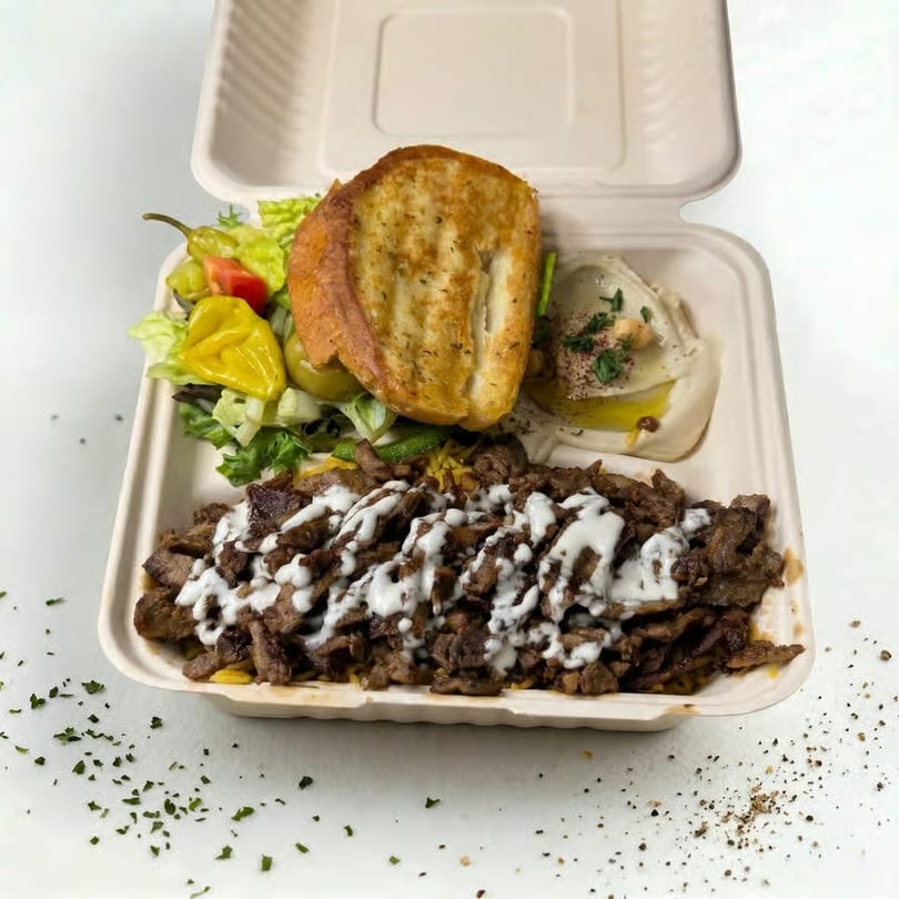 Takeout container with shawarma, hummus, salad, and toasted bread on a white surface.